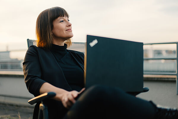 Eine Frau sitzt mit ihrem Laptop auf dem Balkon und arbeitet.